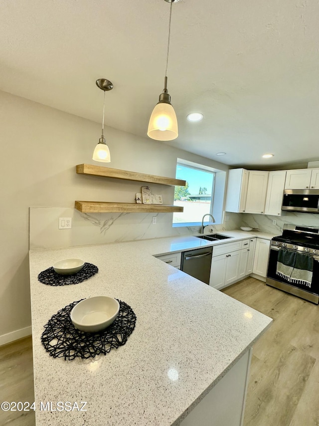 kitchen featuring kitchen peninsula, appliances with stainless steel finishes, sink, pendant lighting, and white cabinetry