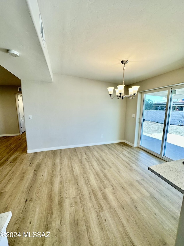 spare room featuring a chandelier and light wood-type flooring