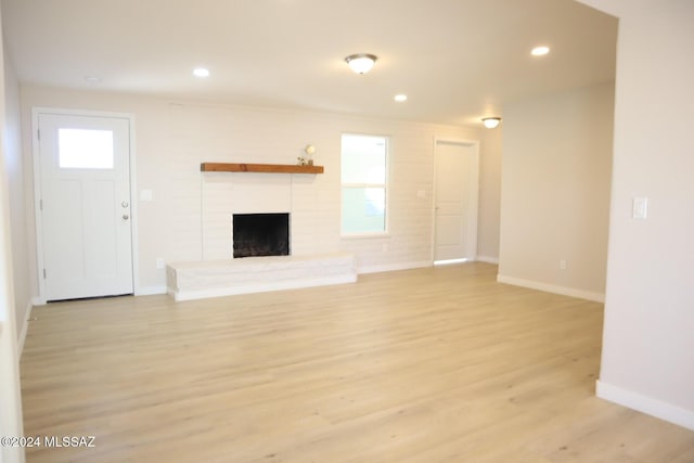 unfurnished living room featuring light wood-type flooring and a brick fireplace