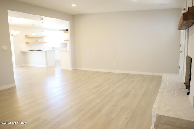 unfurnished living room with a fireplace, light wood-type flooring, and a notable chandelier