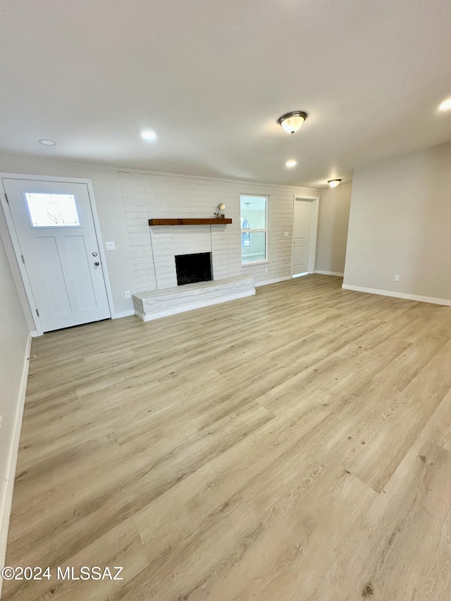 unfurnished living room with light hardwood / wood-style flooring and a brick fireplace