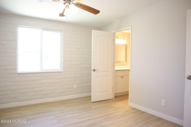 unfurnished bedroom with connected bathroom, ceiling fan, light hardwood / wood-style flooring, and brick wall