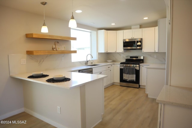 kitchen with kitchen peninsula, stainless steel appliances, sink, white cabinetry, and hanging light fixtures