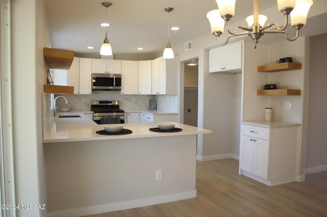 kitchen with stainless steel appliances, kitchen peninsula, a chandelier, decorative light fixtures, and white cabinets