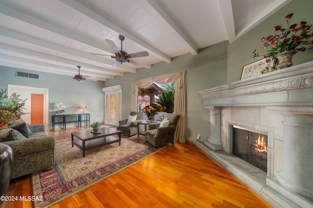 living room featuring a tile fireplace, beam ceiling, hardwood / wood-style flooring, and ceiling fan