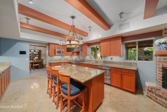 kitchen featuring a breakfast bar, light stone countertops, a brick fireplace, a center island with sink, and appliances with stainless steel finishes