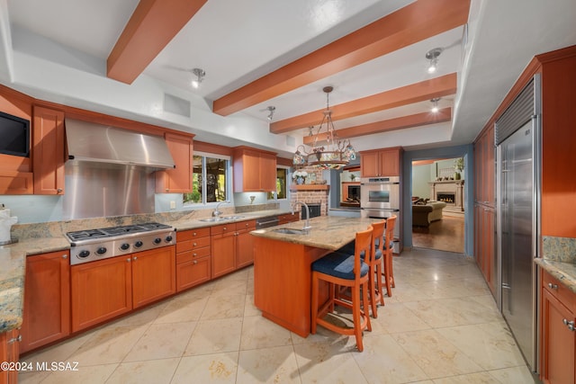 kitchen featuring wall chimney range hood, stainless steel appliances, light stone counters, and an island with sink