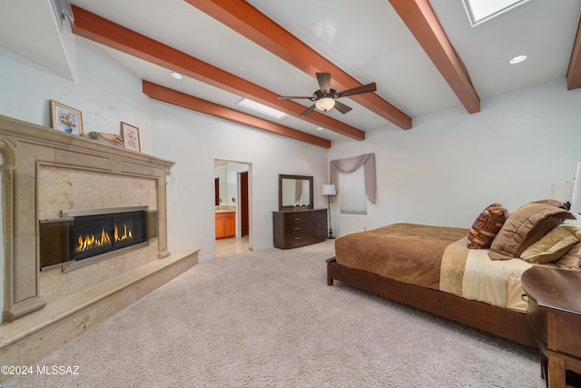 bedroom featuring ensuite bath, ceiling fan, a premium fireplace, beamed ceiling, and light colored carpet