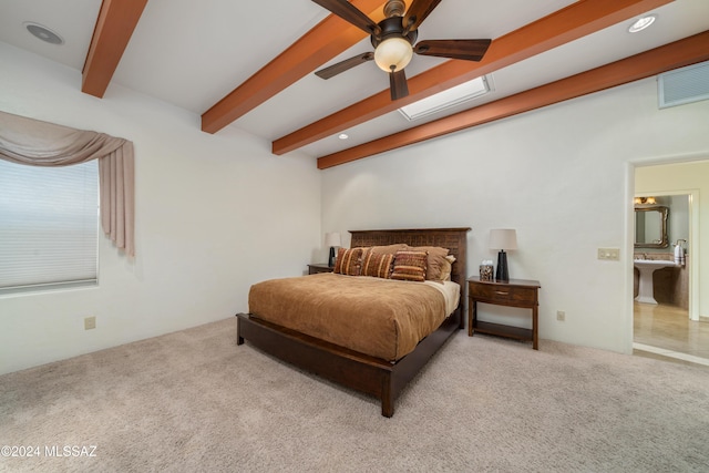 bedroom featuring light carpet, ensuite bath, ceiling fan, and beamed ceiling