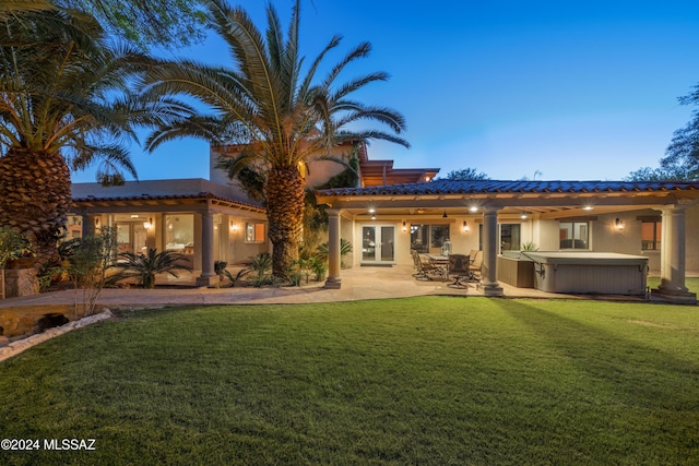 back house at dusk with a lawn, ceiling fan, french doors, a hot tub, and a patio