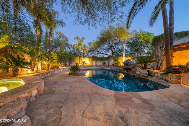 pool at dusk with an in ground hot tub