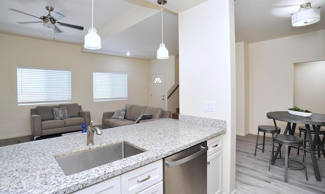 kitchen with sink, hanging light fixtures, stainless steel dishwasher, light stone counters, and white cabinetry