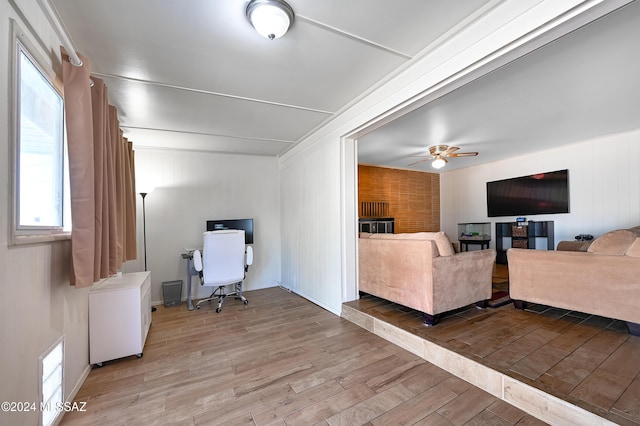 living room with ceiling fan, light hardwood / wood-style floors, and wood walls