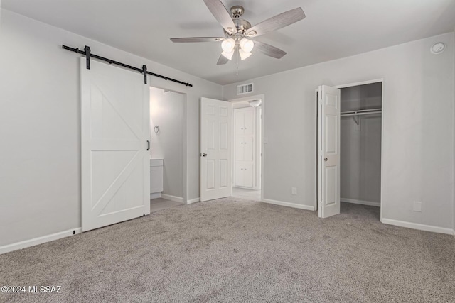 unfurnished bedroom with a barn door, ceiling fan, a closet, and carpet