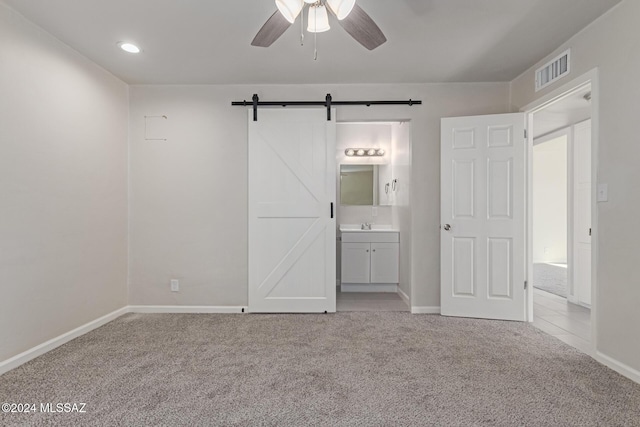 unfurnished bedroom with a barn door, light colored carpet, ensuite bath, and ceiling fan