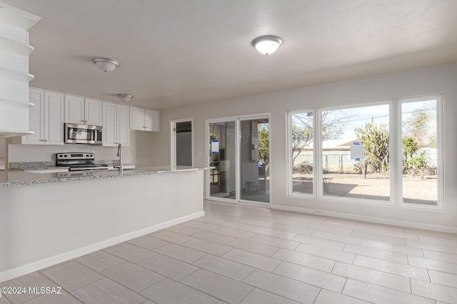 kitchen with kitchen peninsula, light stone counters, stainless steel appliances, sink, and white cabinets