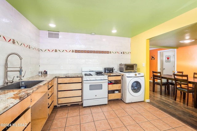 kitchen with sink, light stone counters, light hardwood / wood-style flooring, washer / clothes dryer, and white gas range oven