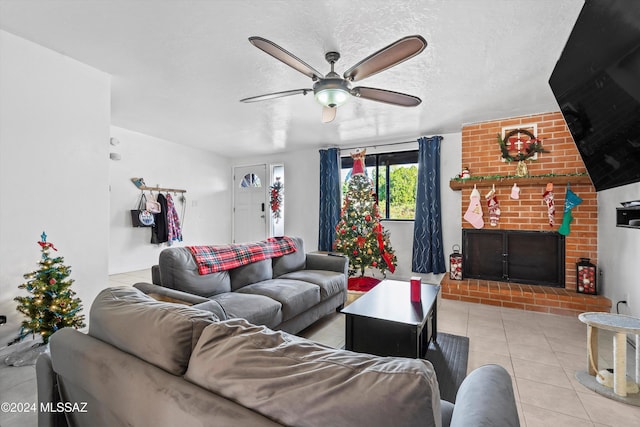 living room with ceiling fan, light tile patterned floors, a textured ceiling, and a brick fireplace