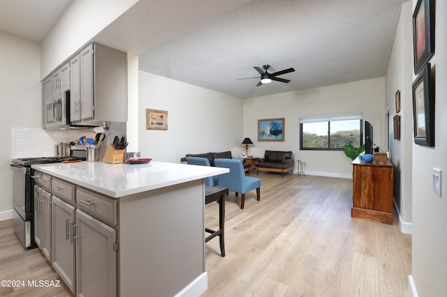 kitchen with appliances with stainless steel finishes, a breakfast bar, gray cabinetry, decorative backsplash, and a textured ceiling