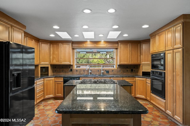 kitchen with a skylight, a kitchen island, dark stone counters, and black appliances