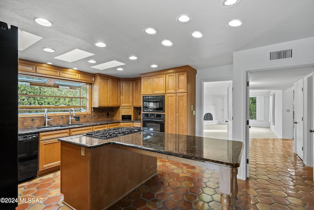 kitchen with a skylight, dark stone countertops, a kitchen island, and black appliances