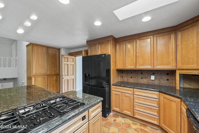 kitchen with backsplash, a skylight, dark stone counters, black appliances, and light tile patterned floors