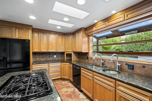 kitchen featuring a skylight, backsplash, dark stone countertops, light tile patterned floors, and black appliances