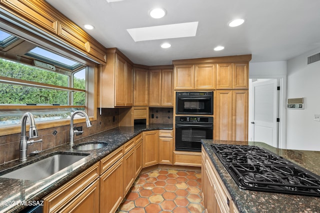 kitchen with a skylight, sink, dark stone countertops, and black appliances