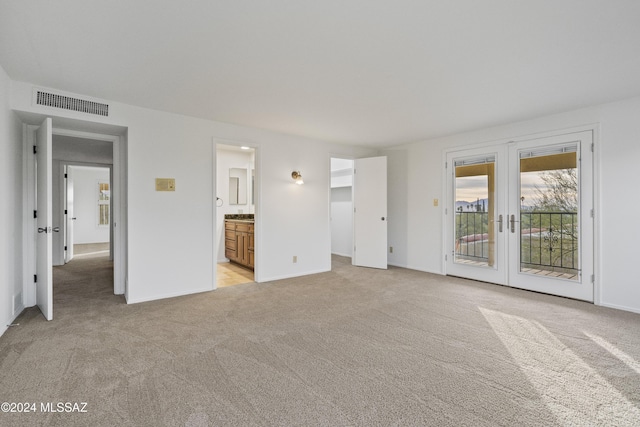 interior space featuring access to exterior, ensuite bathroom, french doors, and light colored carpet