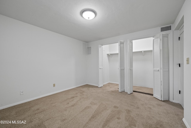 unfurnished bedroom featuring light colored carpet and multiple closets