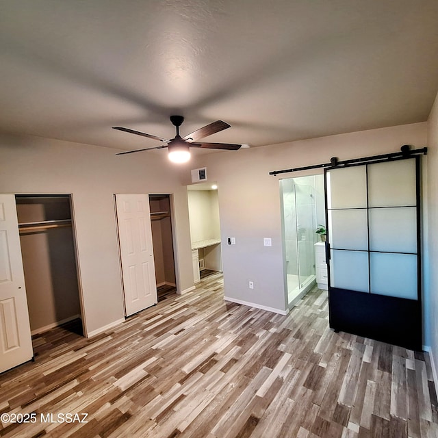 unfurnished bedroom with ceiling fan, a barn door, hardwood / wood-style floors, and ensuite bath