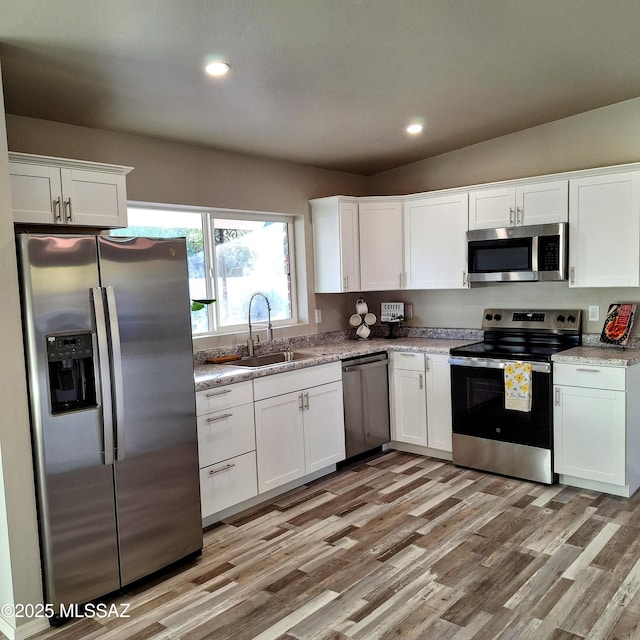 kitchen featuring vaulted ceiling, stainless steel appliances, light hardwood / wood-style floors, and white cabinets