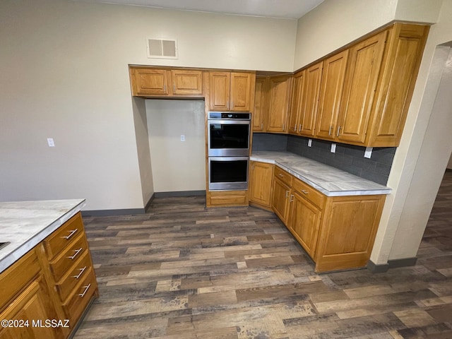 kitchen featuring dark hardwood / wood-style flooring, stainless steel double oven, and backsplash