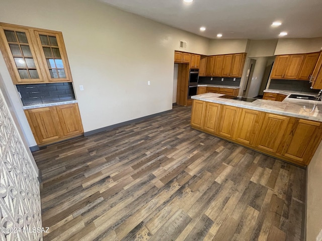 kitchen with dark wood-type flooring, black appliances, sink, decorative backsplash, and kitchen peninsula