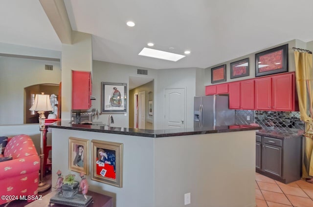 kitchen with a skylight, kitchen peninsula, stainless steel fridge, decorative backsplash, and light tile patterned floors