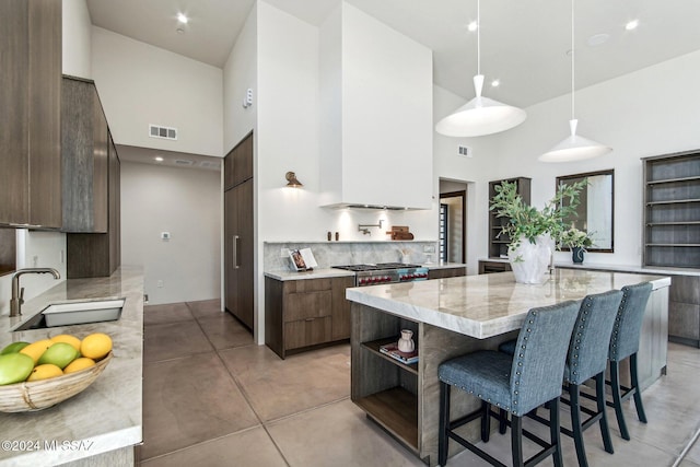 kitchen with a towering ceiling, light stone counters, sink, decorative light fixtures, and a breakfast bar area