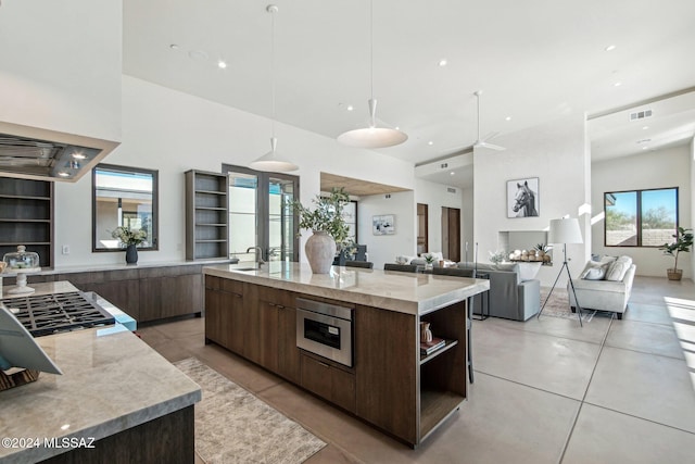 kitchen featuring a large island with sink, sink, decorative light fixtures, light stone counters, and dark brown cabinets