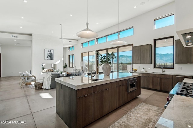 kitchen with stainless steel microwave, sink, hanging light fixtures, a high ceiling, and an island with sink