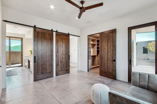 bedroom with ensuite bathroom, a walk in closet, ceiling fan, a barn door, and access to exterior