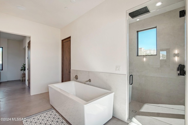 bathroom featuring plus walk in shower, concrete floors, and tile walls