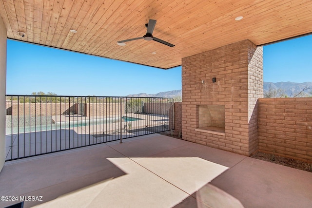 view of patio / terrace with an outdoor brick fireplace, a mountain view, ceiling fan, and a fenced in pool