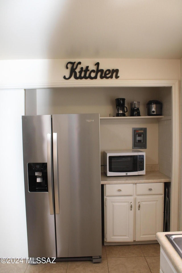 kitchen featuring stainless steel fridge with ice dispenser, light tile patterned floors, and white cabinetry