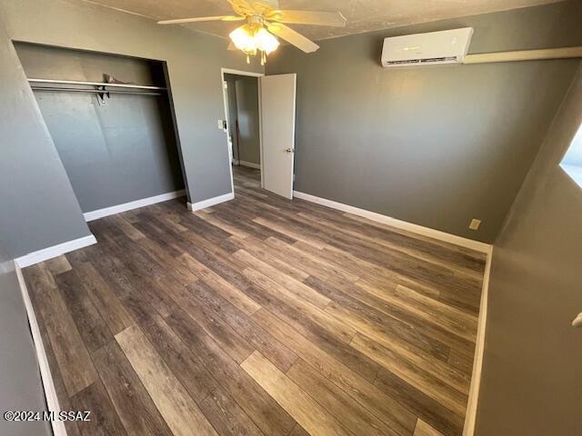 unfurnished bedroom with ceiling fan, dark hardwood / wood-style flooring, a wall unit AC, and a closet