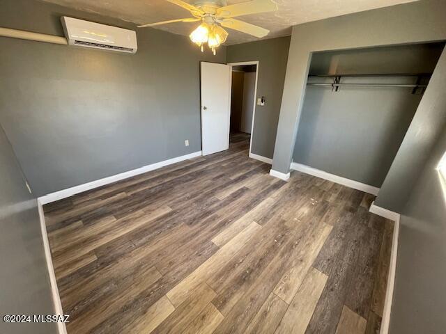 unfurnished bedroom with a wall mounted air conditioner, a closet, dark wood-type flooring, and ceiling fan