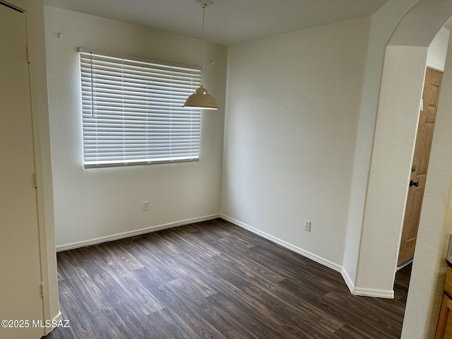 empty room featuring dark wood-style floors, arched walkways, and baseboards