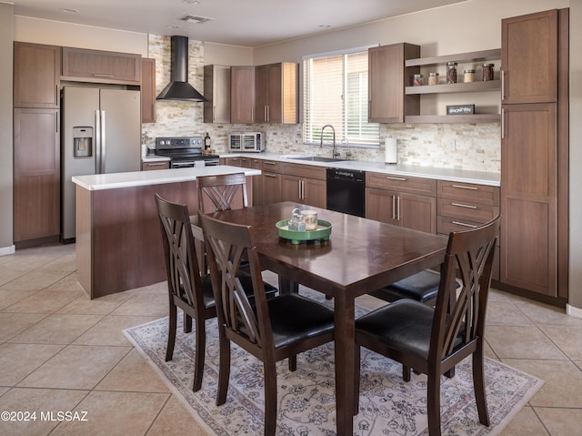 kitchen with sink, wall chimney exhaust hood, light tile patterned floors, a kitchen island, and appliances with stainless steel finishes