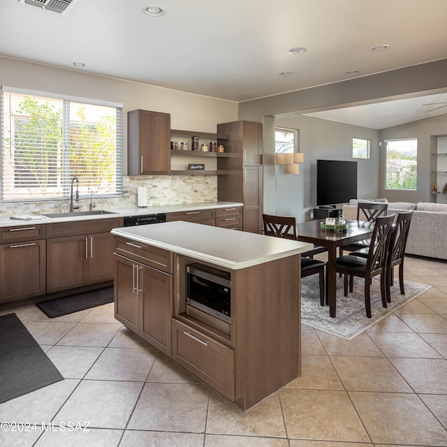 kitchen featuring decorative backsplash, sink, light tile patterned floors, a kitchen island, and stainless steel microwave