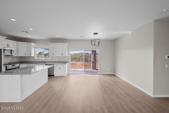 kitchen featuring hanging light fixtures, light hardwood / wood-style flooring, light stone counters, white cabinetry, and stainless steel appliances