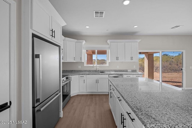 kitchen with sink, stainless steel appliances, light stone counters, light hardwood / wood-style flooring, and white cabinets