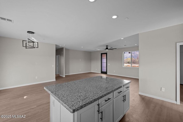 kitchen with light stone countertops, ceiling fan, white cabinets, a center island, and hanging light fixtures